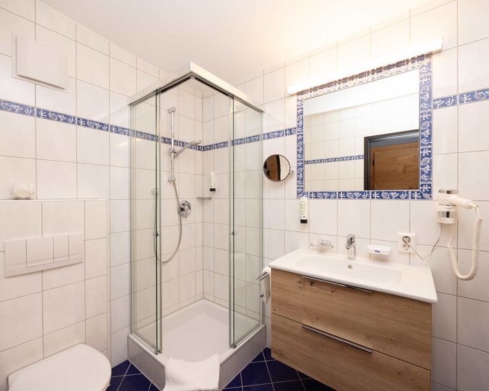 Modernes Badezimmer mit Dusche, großem Spiegel und Holzmöbeln.