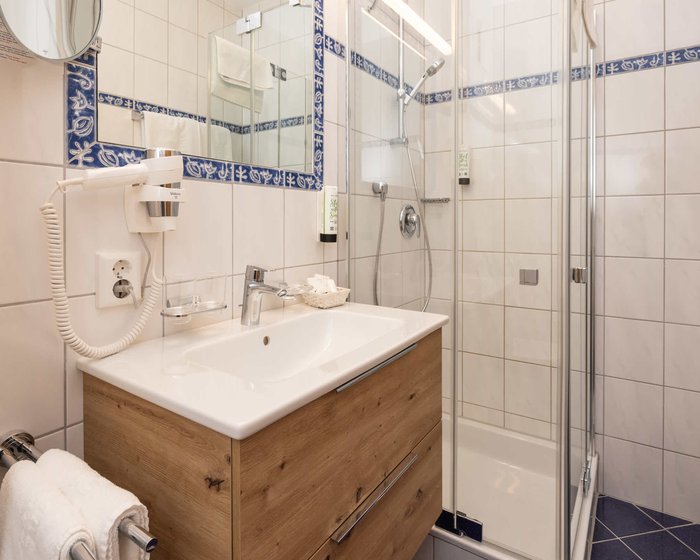 Helles Badezimmer mit Dusche, Holzwaschtisch und blauen Fliesen.