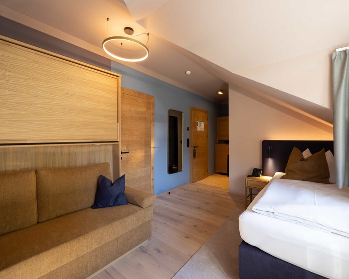 Einzelzimmer mit Bett, Schreibtisch und offener Garderobe.