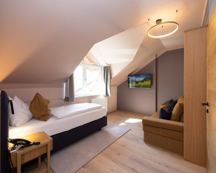 Familienzimmer Comfort mit Einzelbett und Sofabereich unter Dachschräge.
