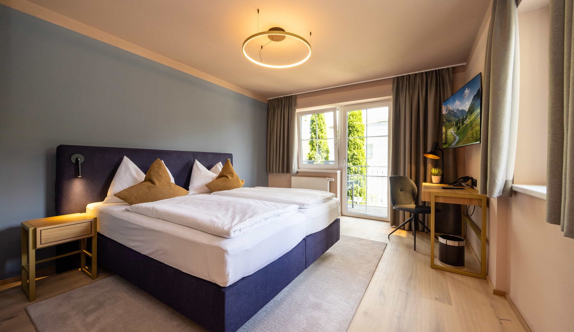 Doppelzimmer mit großem Bett, Schreibtisch und Balkonfenstern.