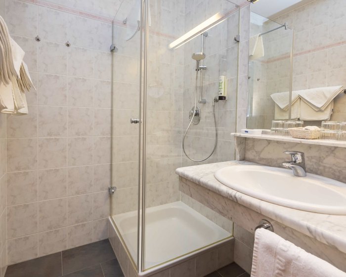 Badezimmer mit Glasdusche, Waschtisch aus Marmor und Spiegel.