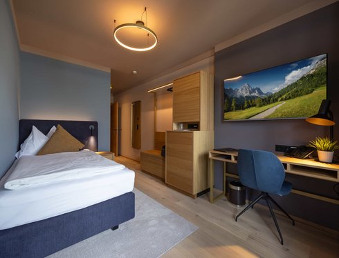 Einzelzimmer mit großem Bett, Schreibtisch und TV an der Wand.