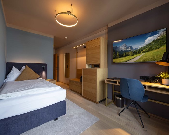 Einzelzimmer mit großem Bett, Schreibtisch und TV an der Wand.