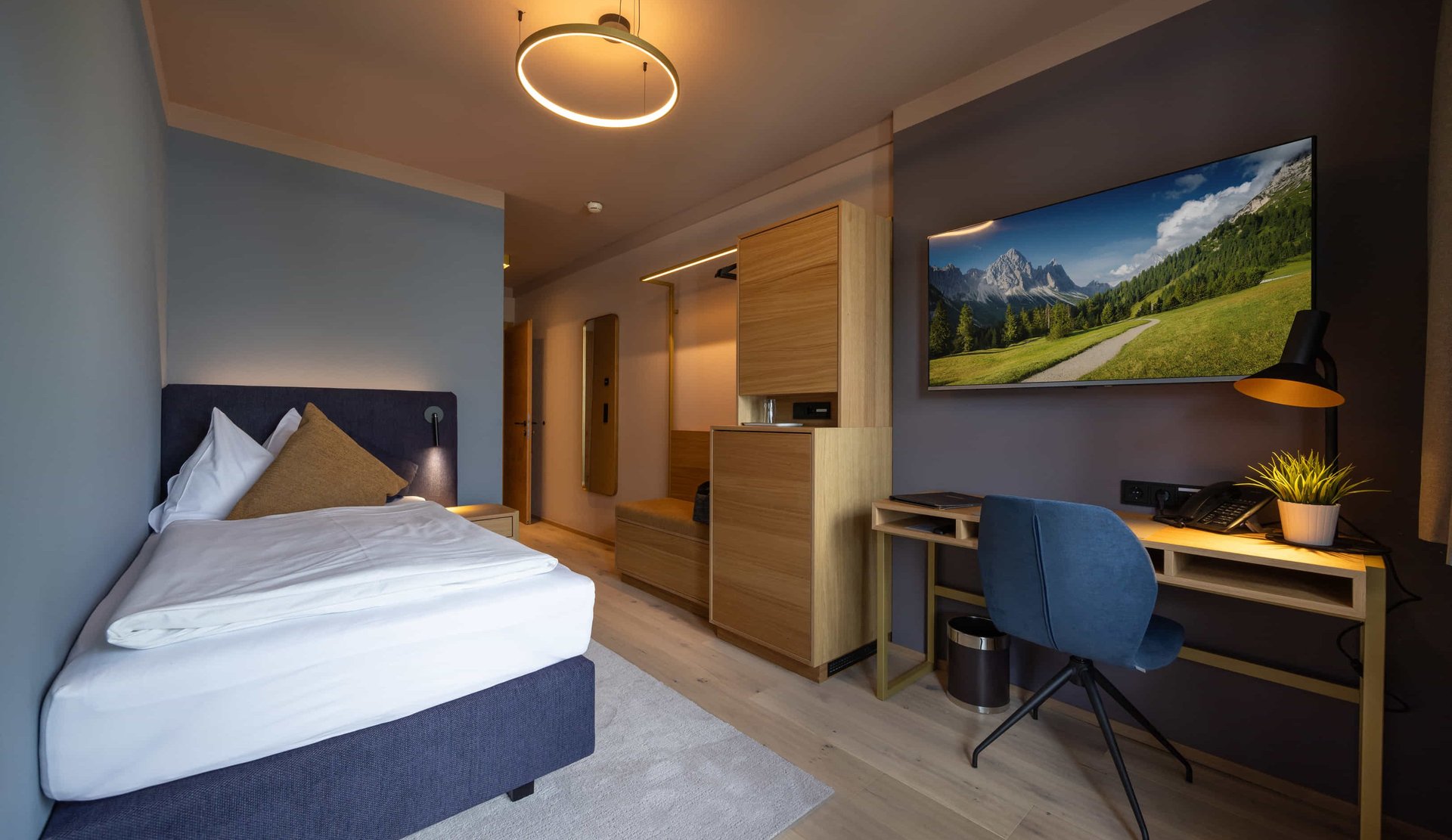 Einzelzimmer mit großem Bett, Schreibtisch und TV an der Wand.