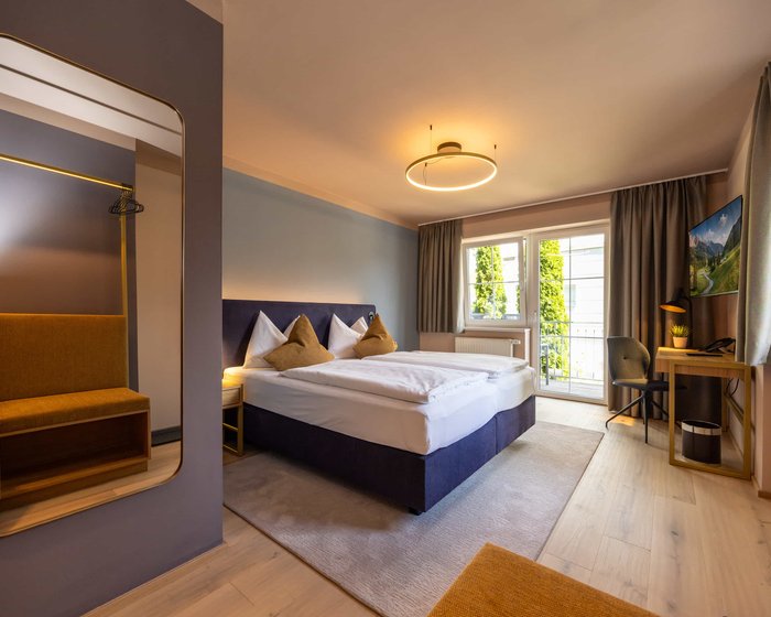 Doppelzimmer mit großem Spiegel, Sitzbank und modernem Bett.